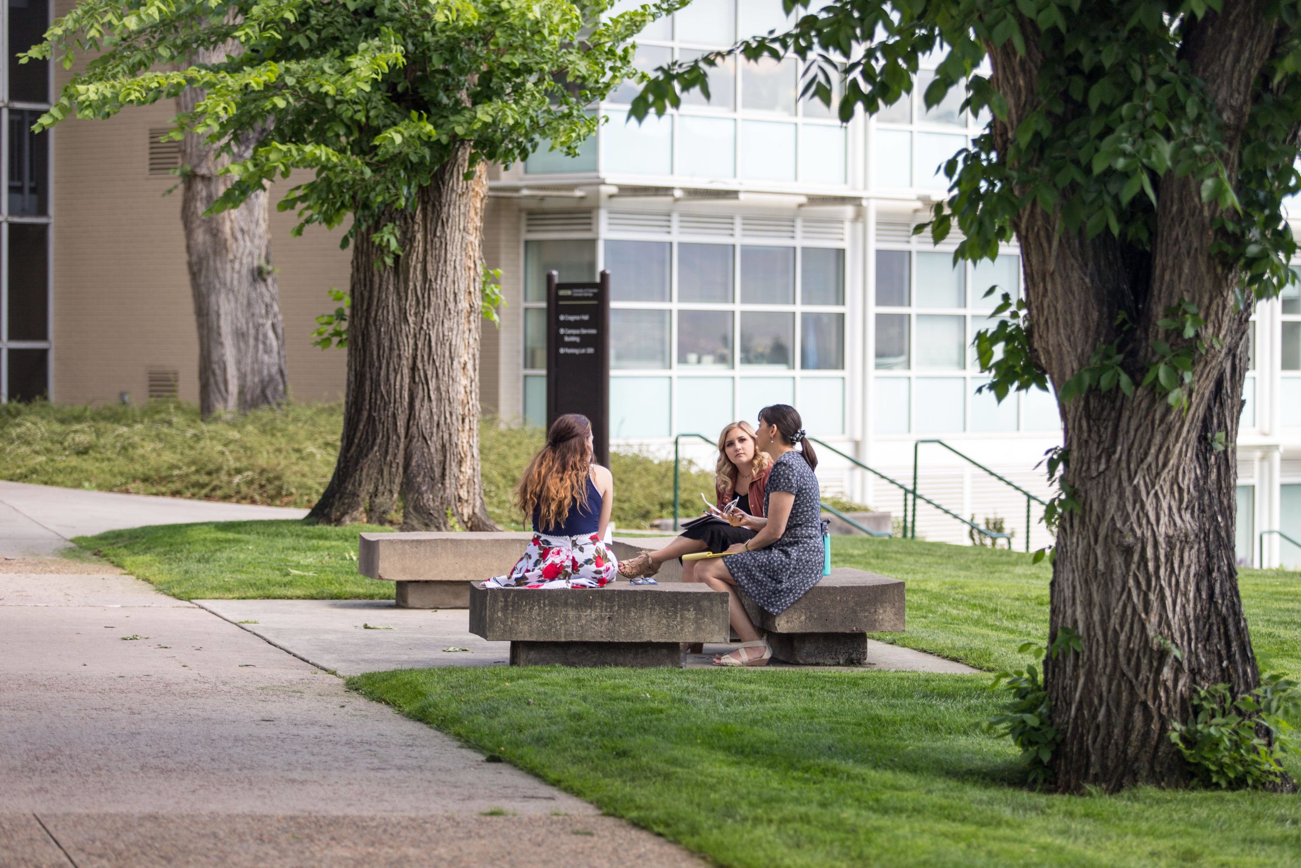 Photo of students sitting on a bench outside a campus building.